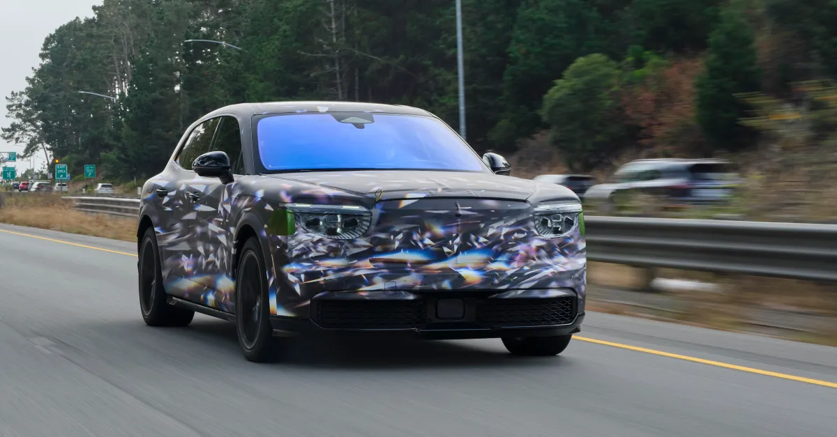 Camouflaged luxury SUV prototype driving on a divided forest-lined roadway