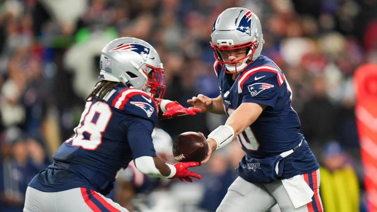 Two New England Patriots players exchange the football during an NFL game.
