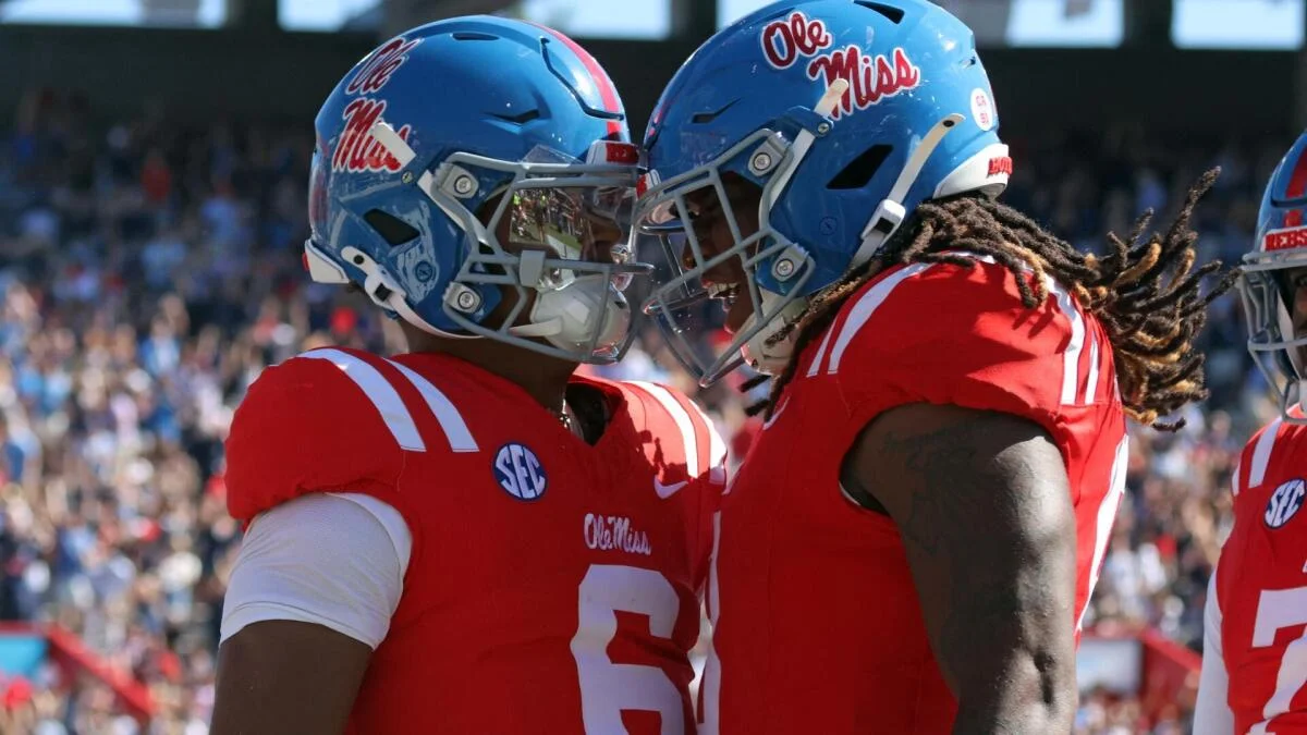 Two Ole Miss football players in red uniforms and blue helmets touch helmets during a game.