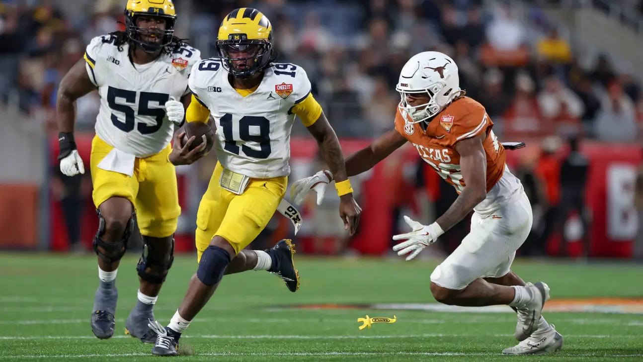College football player in Michigan uniform runs with ball as Texas defender gives chase