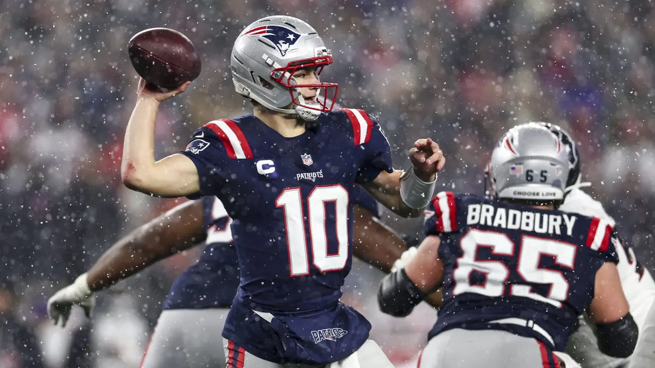 Patriots quarterback throws a football during a snowy game as teammate Bradbury blocks nearby