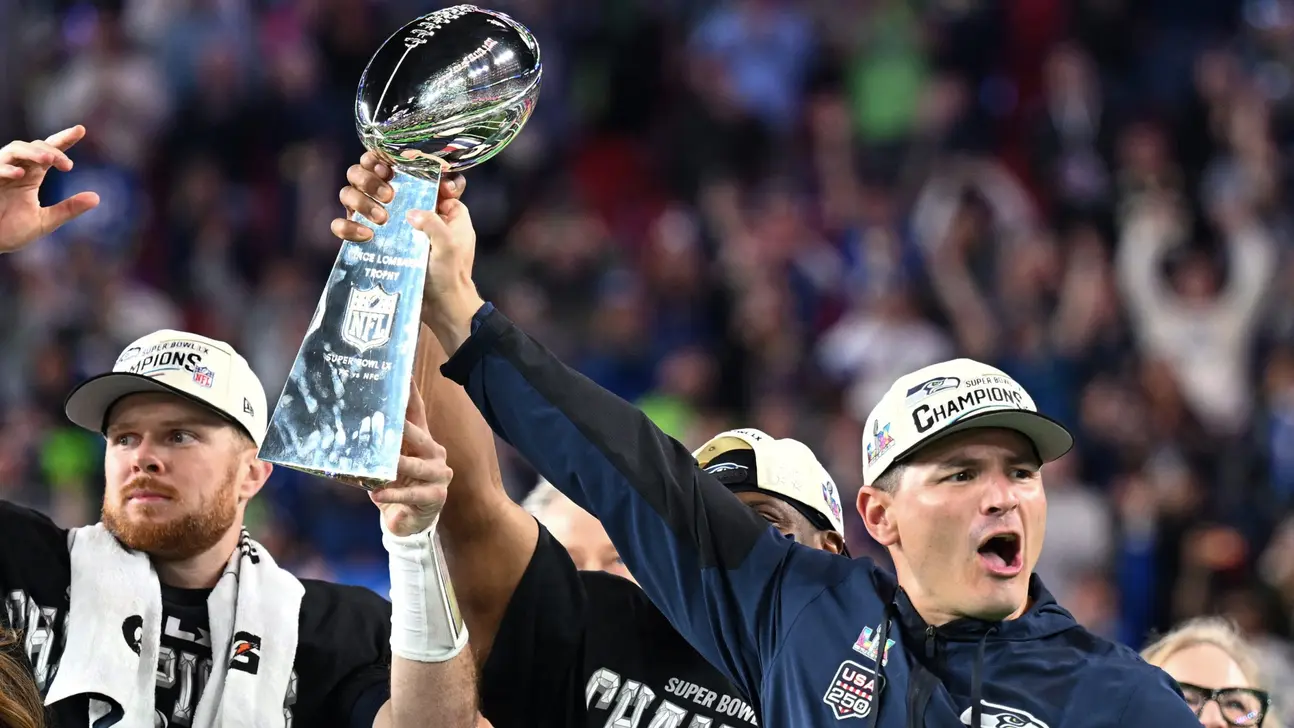 Football players celebrate while holding the Vince Lombardi Trophy amid cheering fans.
