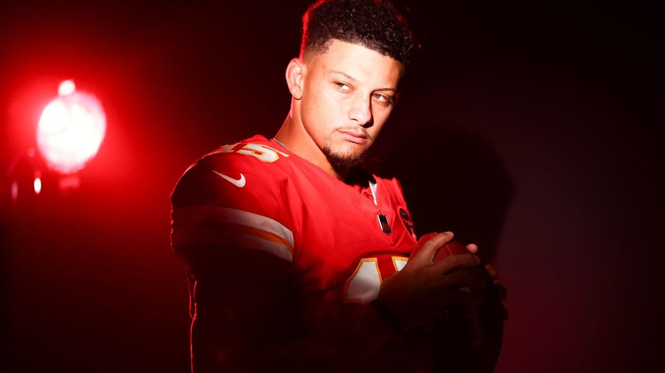 Football player in red jersey cradles a ball under dramatic red lighting.