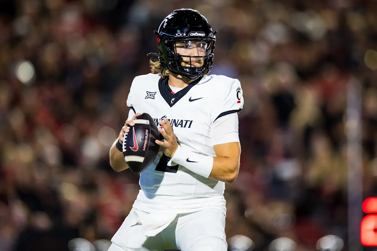 Football player in white Cincinnati uniform holding a football during a nighttime game