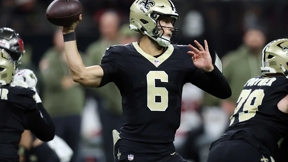 Saints quarterback in black number 6 jersey prepares to throw as teammates block nearby.