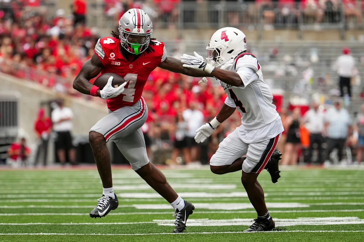 Ohio State football player runs with the ball as a defender reaches toward him.