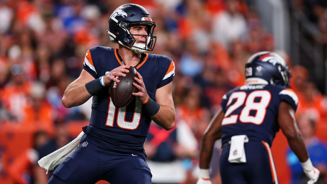 Denver Broncos quarterback in navy number 10 jersey prepares to throw as teammate number 28 runs ahead.