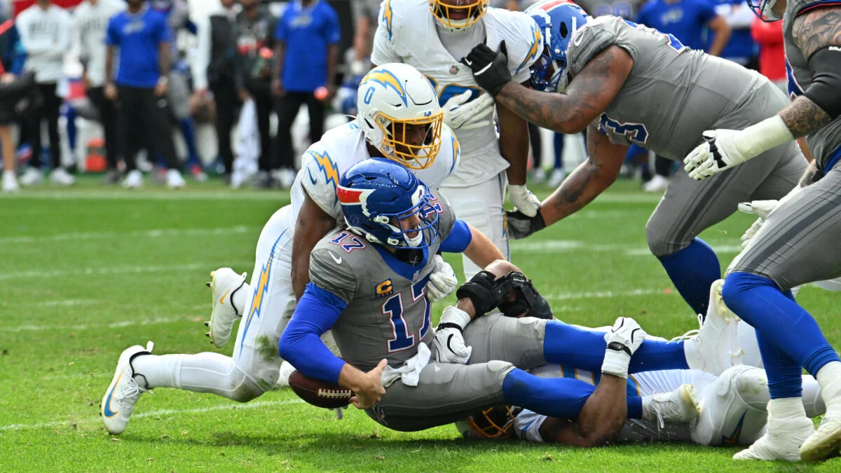 A Chargers defender tackles a Giants player in a gray uniform as other players converge on the field.