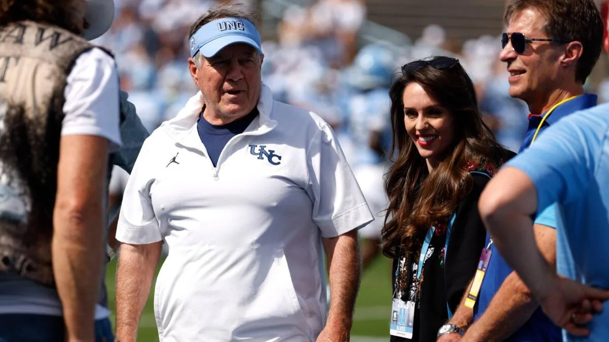 Man in UNC apparel walks beside a woman wearing credentials at a crowded outdoor sporting event