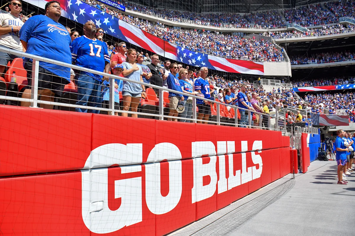 Buffalo Bills fans stand in a stadium beneath a large American flag