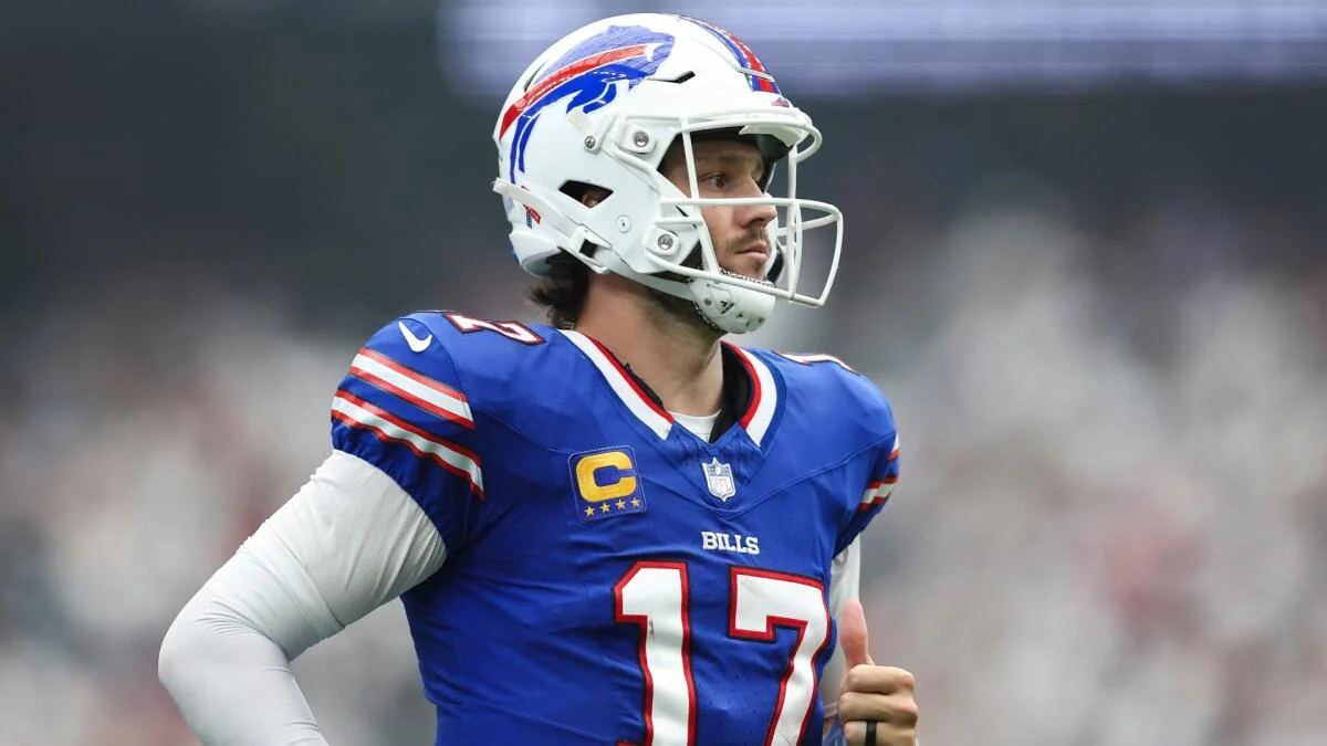 Buffalo Bills quarterback Josh Allen stands on the field wearing a blue uniform and white helmet.