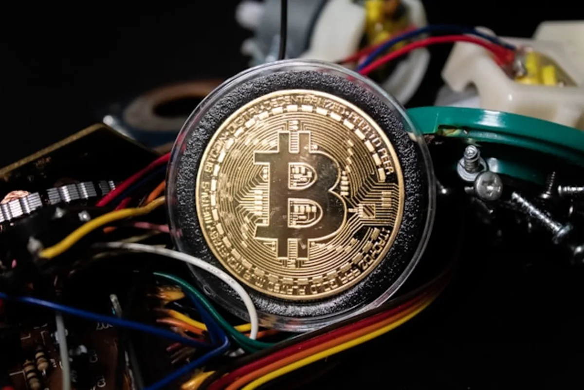 Gold Bitcoin coin resting atop a tangle of colorful electronic wires and components