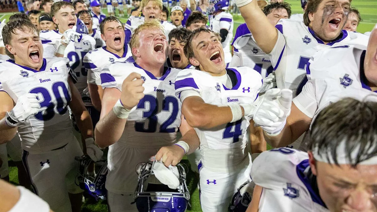 Boerne football players in white and purple uniforms celebrate together on the field after a game.