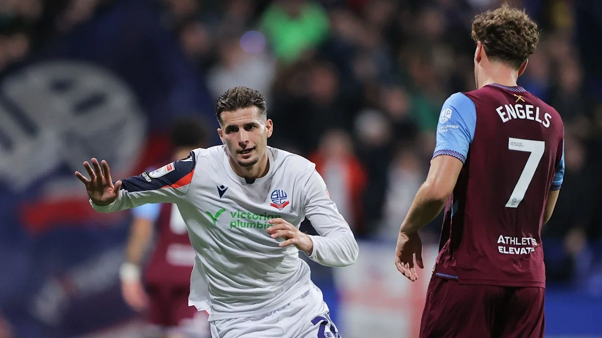 A Bolton player in white runs past an opposing player in claret and blue.
