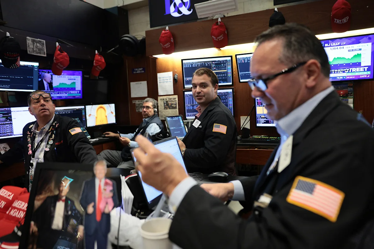Traders work amid market monitors and American flags at a busy exchange floor.