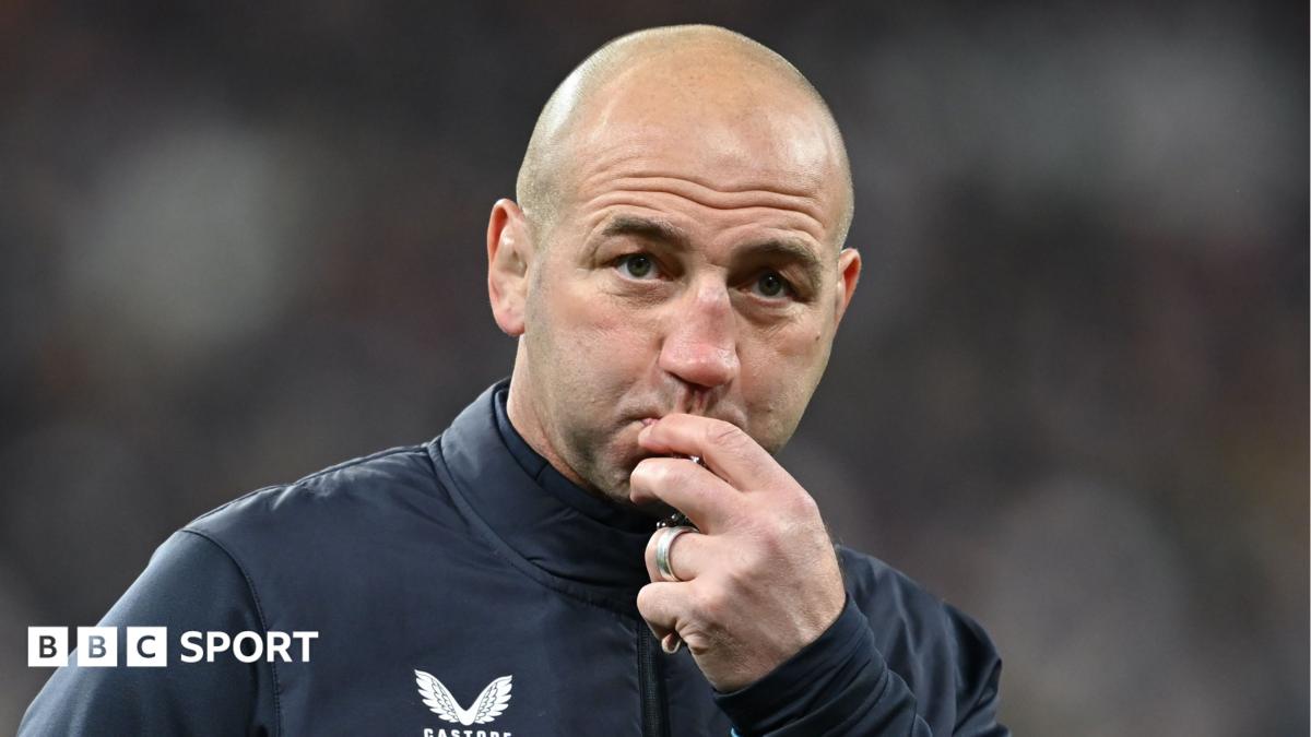 Bald rugby coach touching his lips while wearing a dark training top