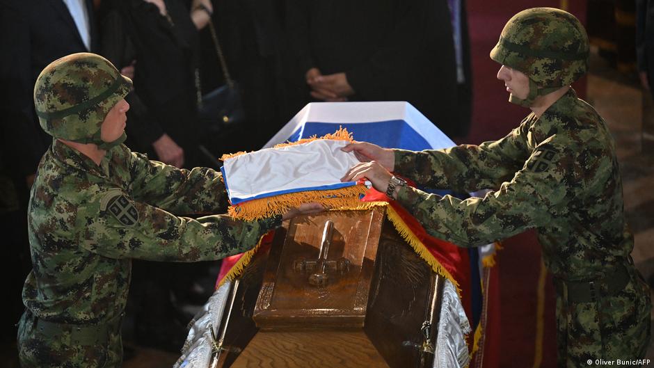 Two camouflage-clad soldiers drape a Serbian flag over a coffin during a funeral ceremony.
