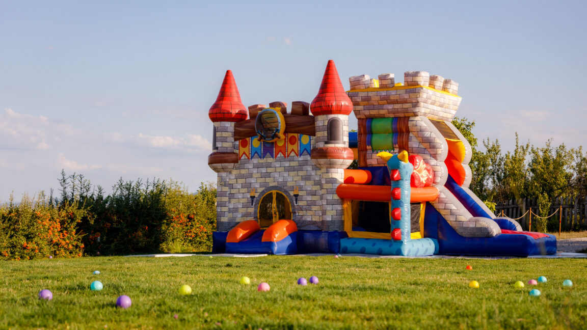 Colorful castle-themed inflatable bouncy castle with slides stands on a grassy field.