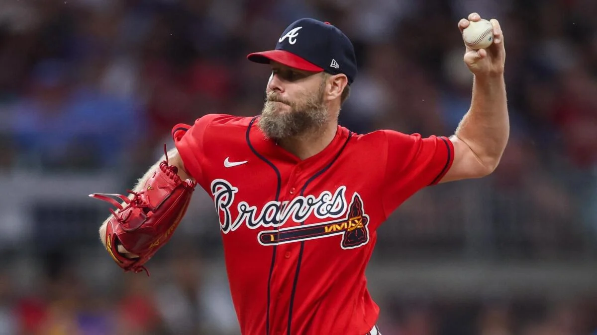 A bearded pitcher in a red Braves uniform raises a baseball during his windup.