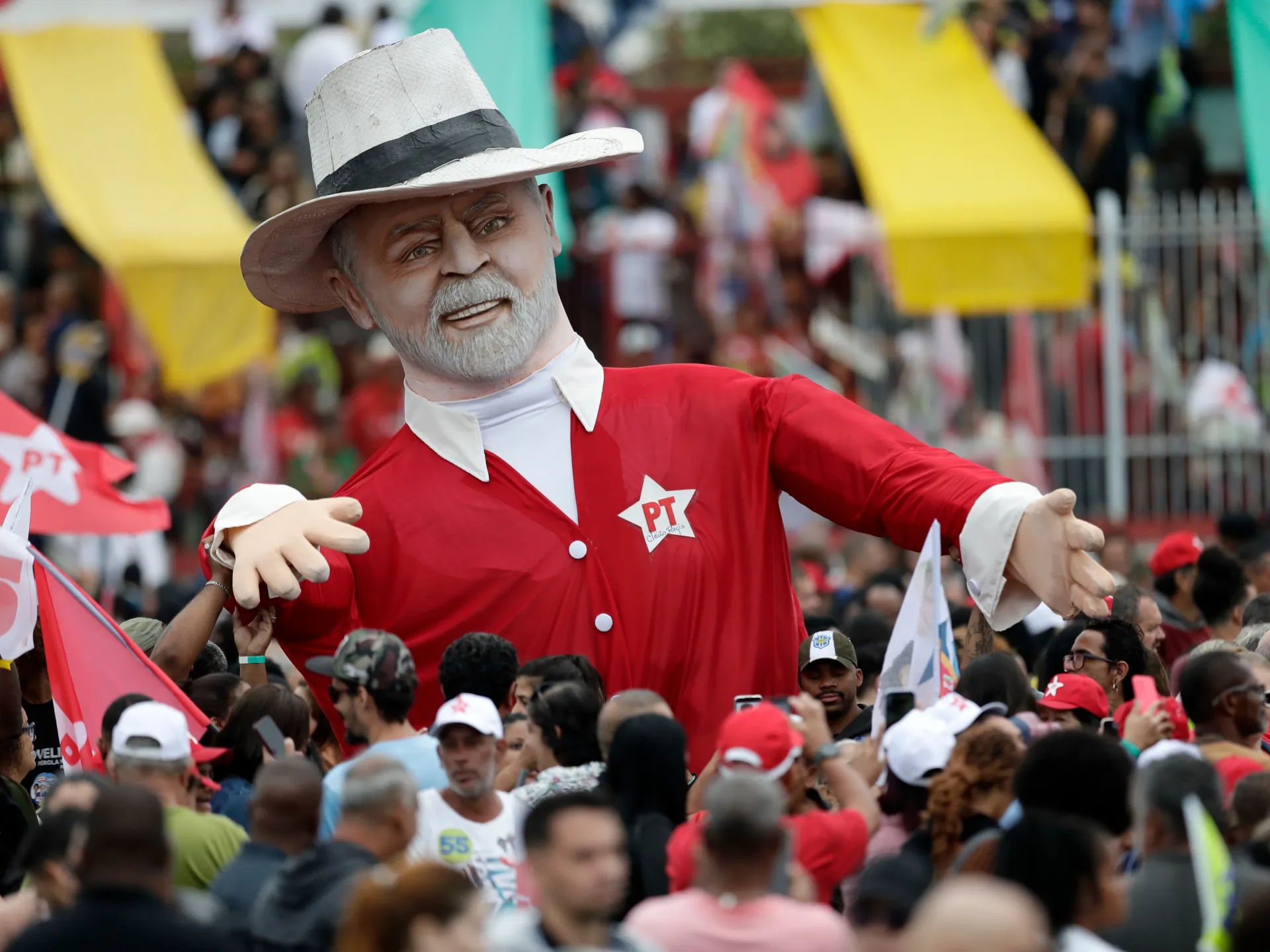 Large bearded political caricature in red costume towers over a dense outdoor crowd.