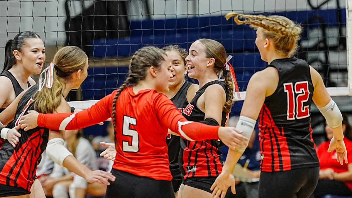High school volleyball players in red and black uniforms gather near the net during a match.
