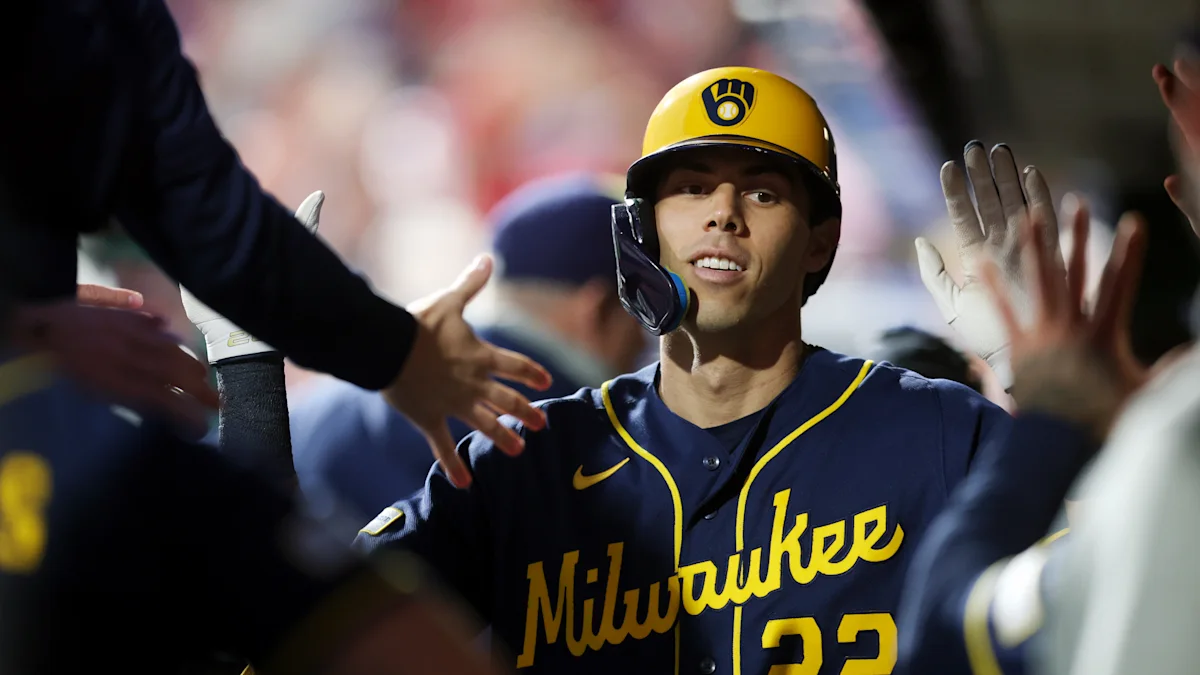 Milwaukee Brewers player in a yellow helmet and navy jersey high-fives people near the dugout.