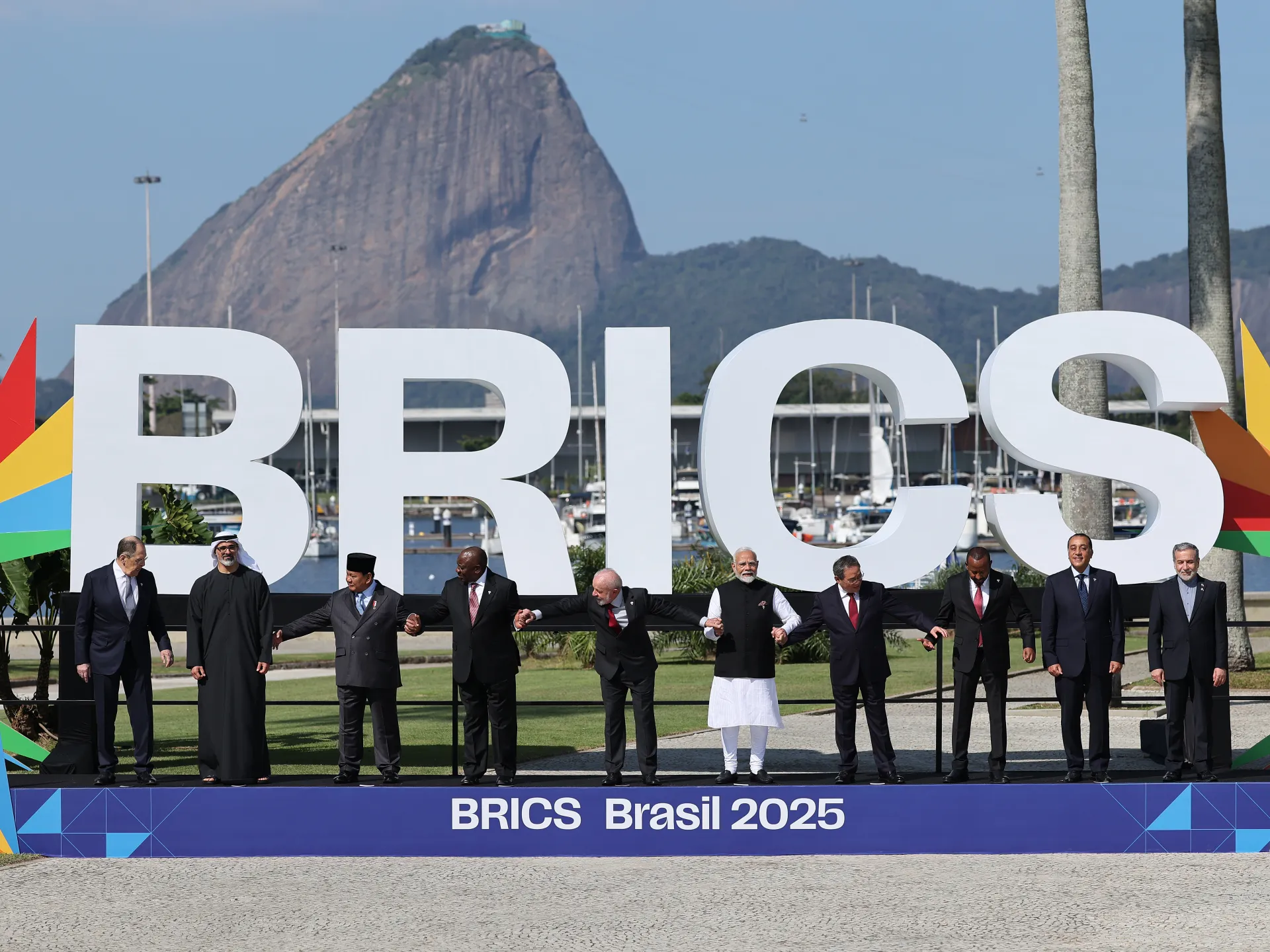 World leaders stand hand-in-hand before large BRICS letters with a mountain and marina behind them.