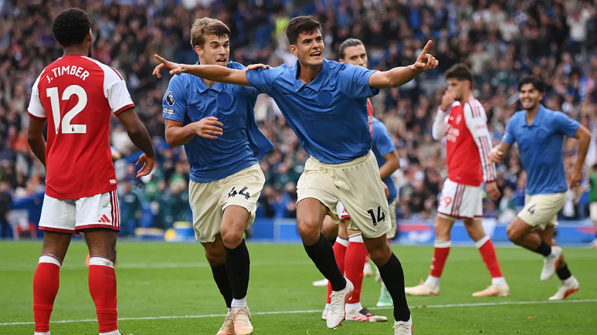 Blue-shirted footballers celebrate as an Arsenal player in red stands nearby during a match