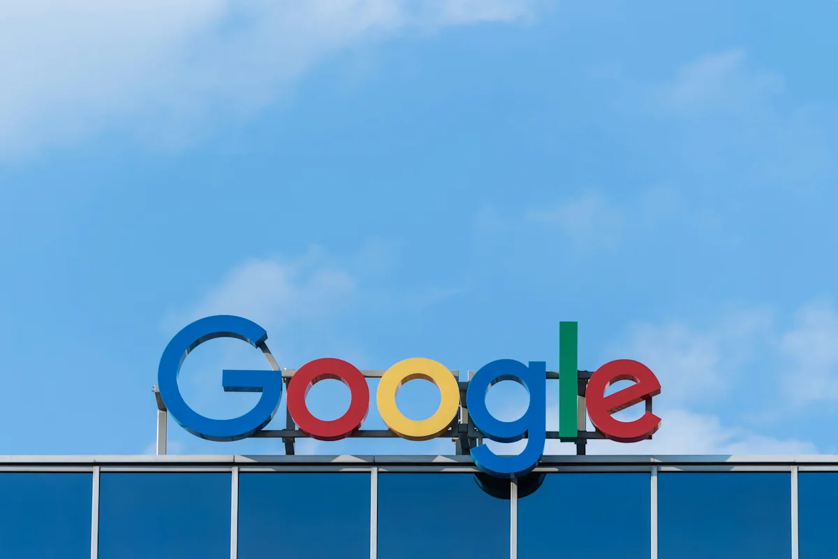 Google logo mounted on a building against a bright blue sky with scattered clouds