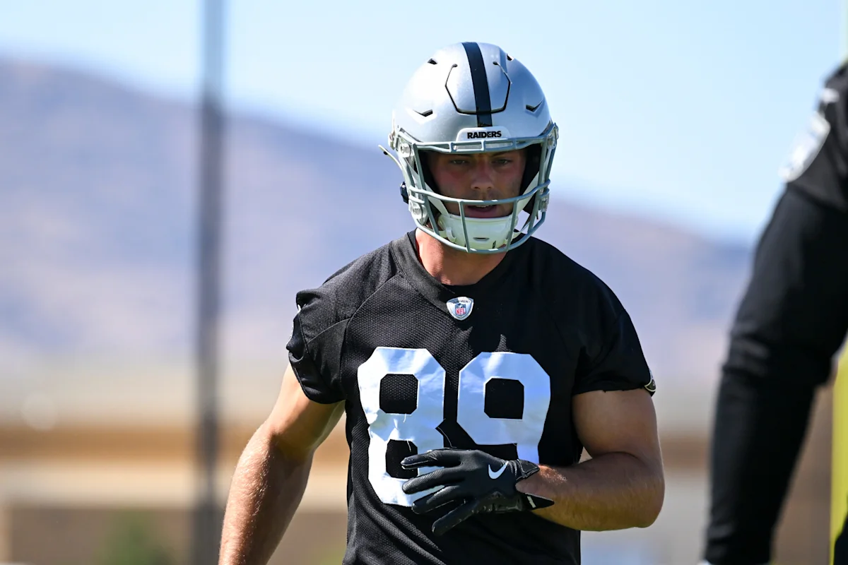 Football player in Raiders uniform and helmet standing on a practice field