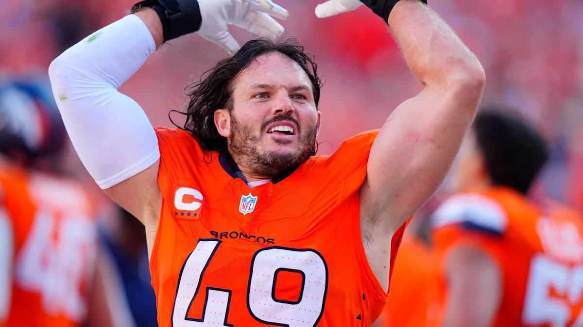A Denver Broncos player in an orange number 49 jersey raises both arms during a game.