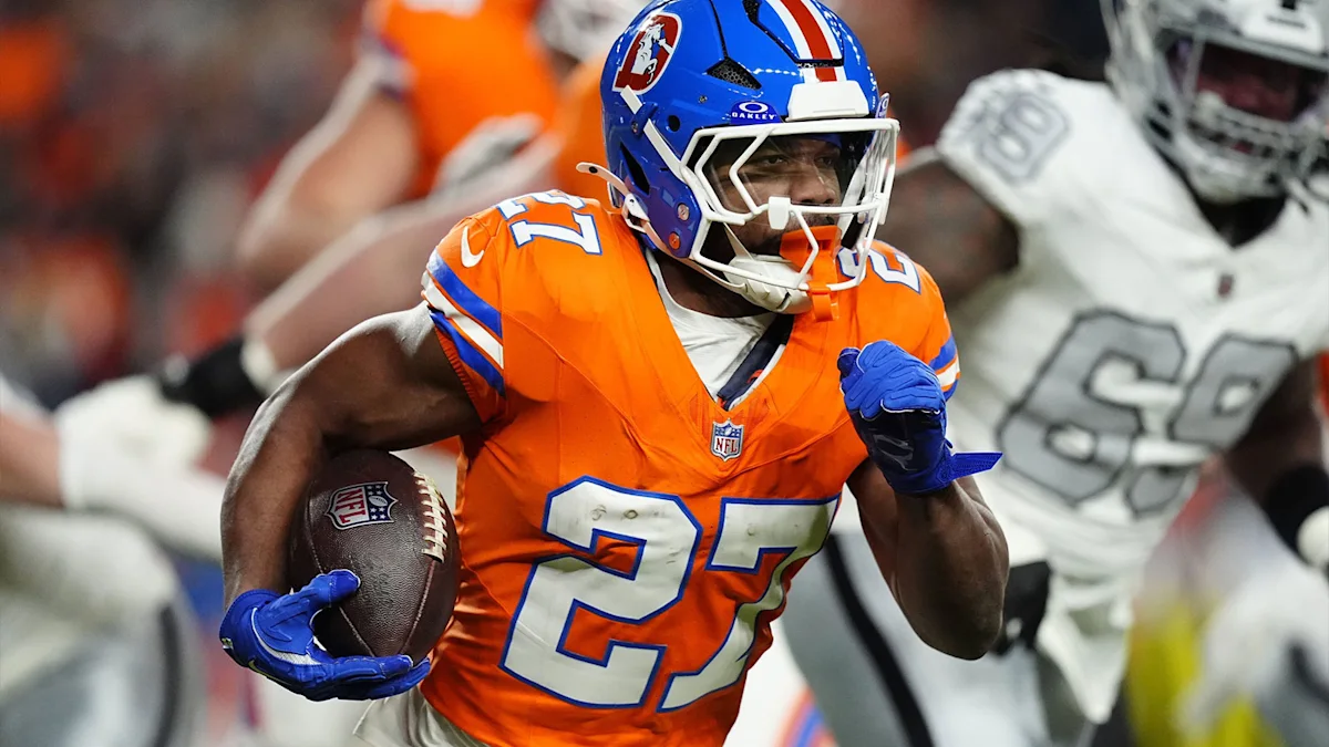 Denver Broncos player in orange jersey and blue helmet runs with a football during a game