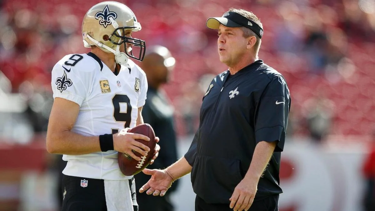 Former Saints quarterback Drew Brees and a Saints coach speak on the sideline during an NFL game.