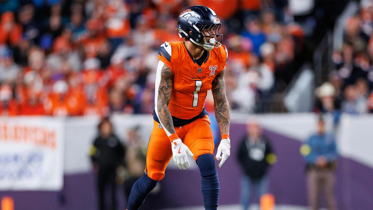 Denver Broncos player in an orange number 1 uniform stands on the field during a game.