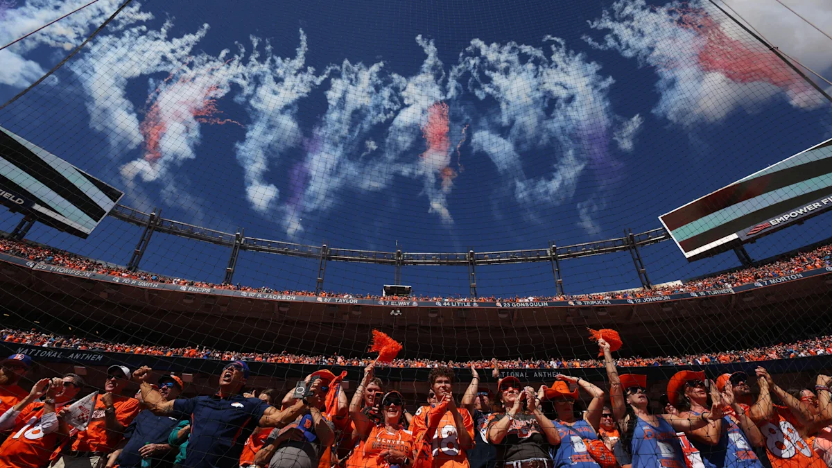 Denver Broncos fans cheer beneath a stadium safety net as clouds drift across the sky.
