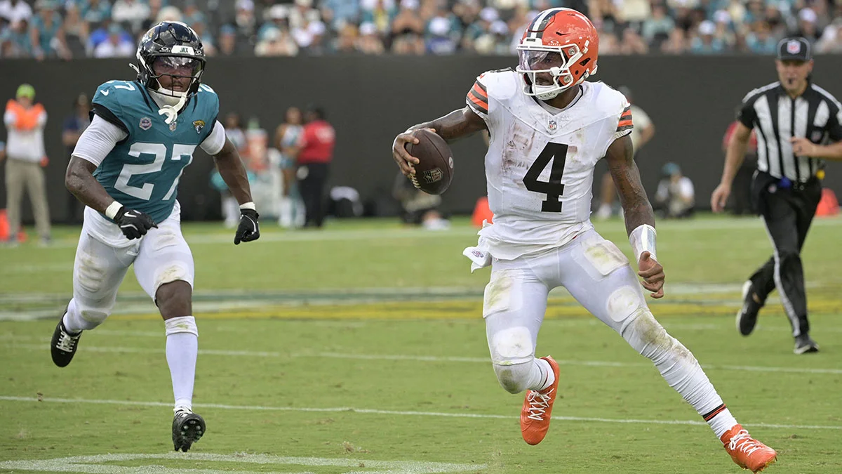 Browns quarterback in white uniform runs with the football as a Jaguars defender pursues him.