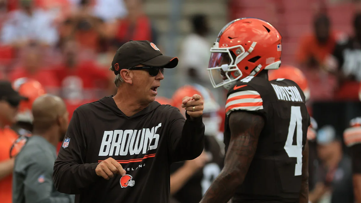Browns coach gestures toward a helmeted player on the sideline during a football game