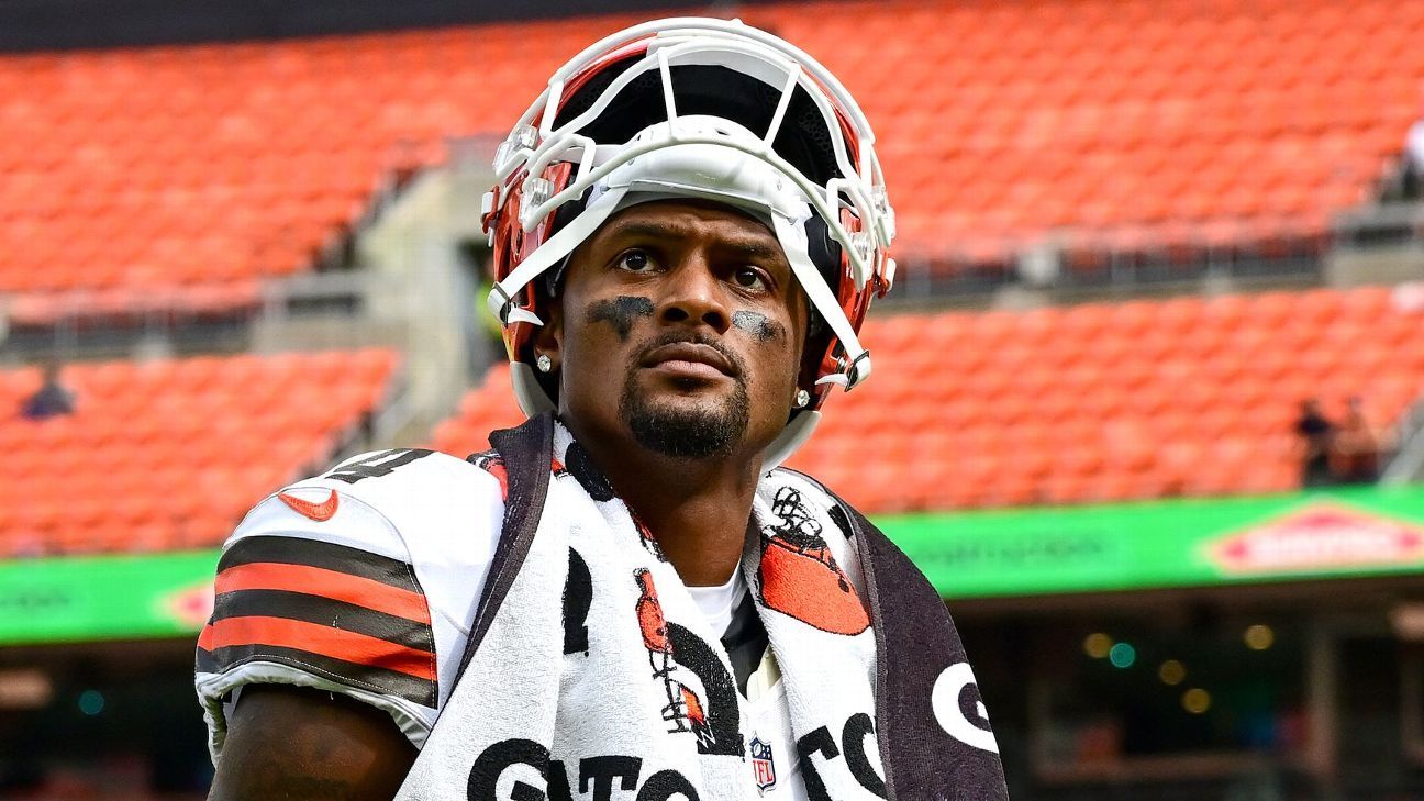 Football player wearing a white helmet and Browns jersey stands on the field.