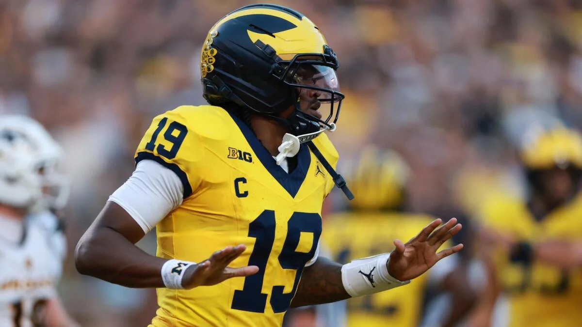 Football player in a Michigan Wolverines uniform gestures on the field during a game.