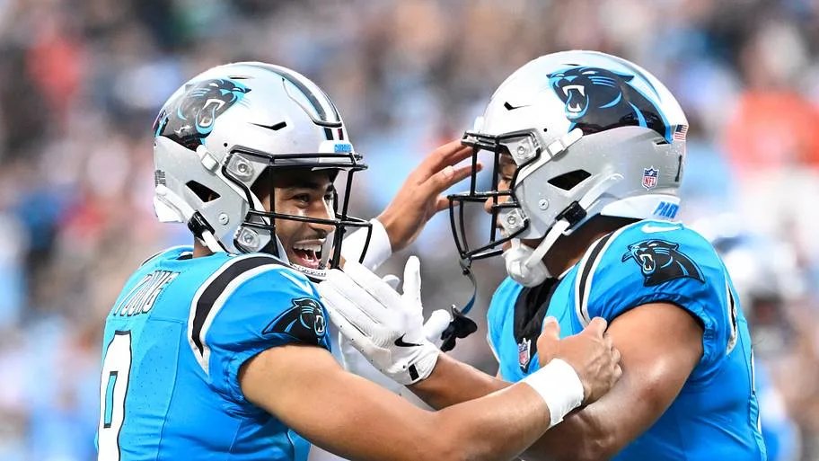 Two Carolina Panthers players in blue uniforms celebrate together on the field, touching helmets.