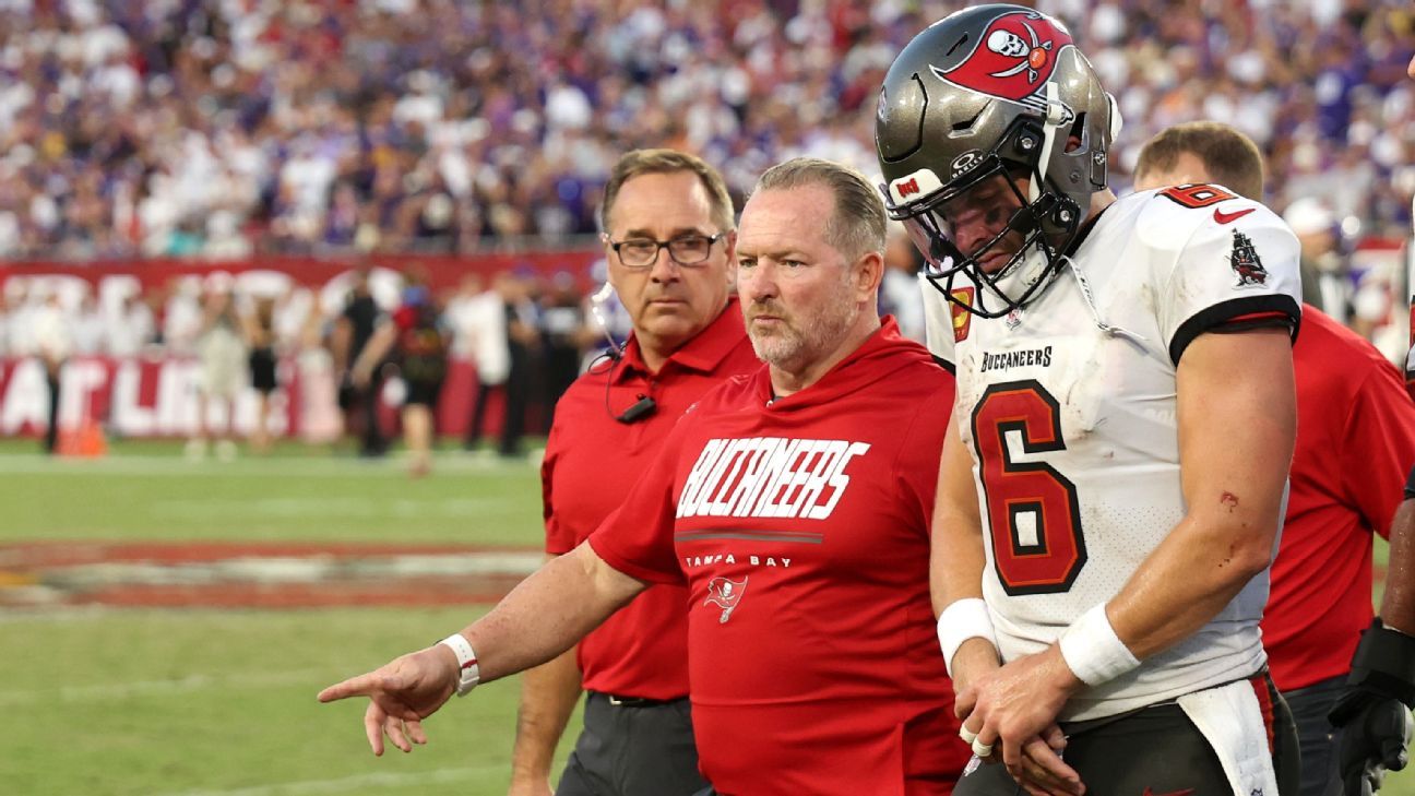 Buccaneers quarterback in a white number 6 jersey walks beside a coach in red.