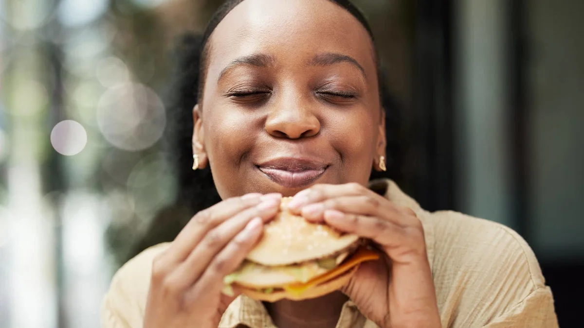 Smiling woman with eyes closed holds a burger in both hands.