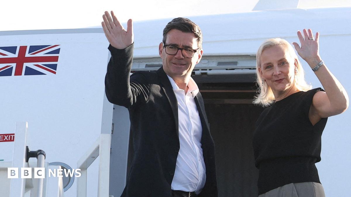A man and woman wave while standing in an aircraft doorway, with a British flag visible.