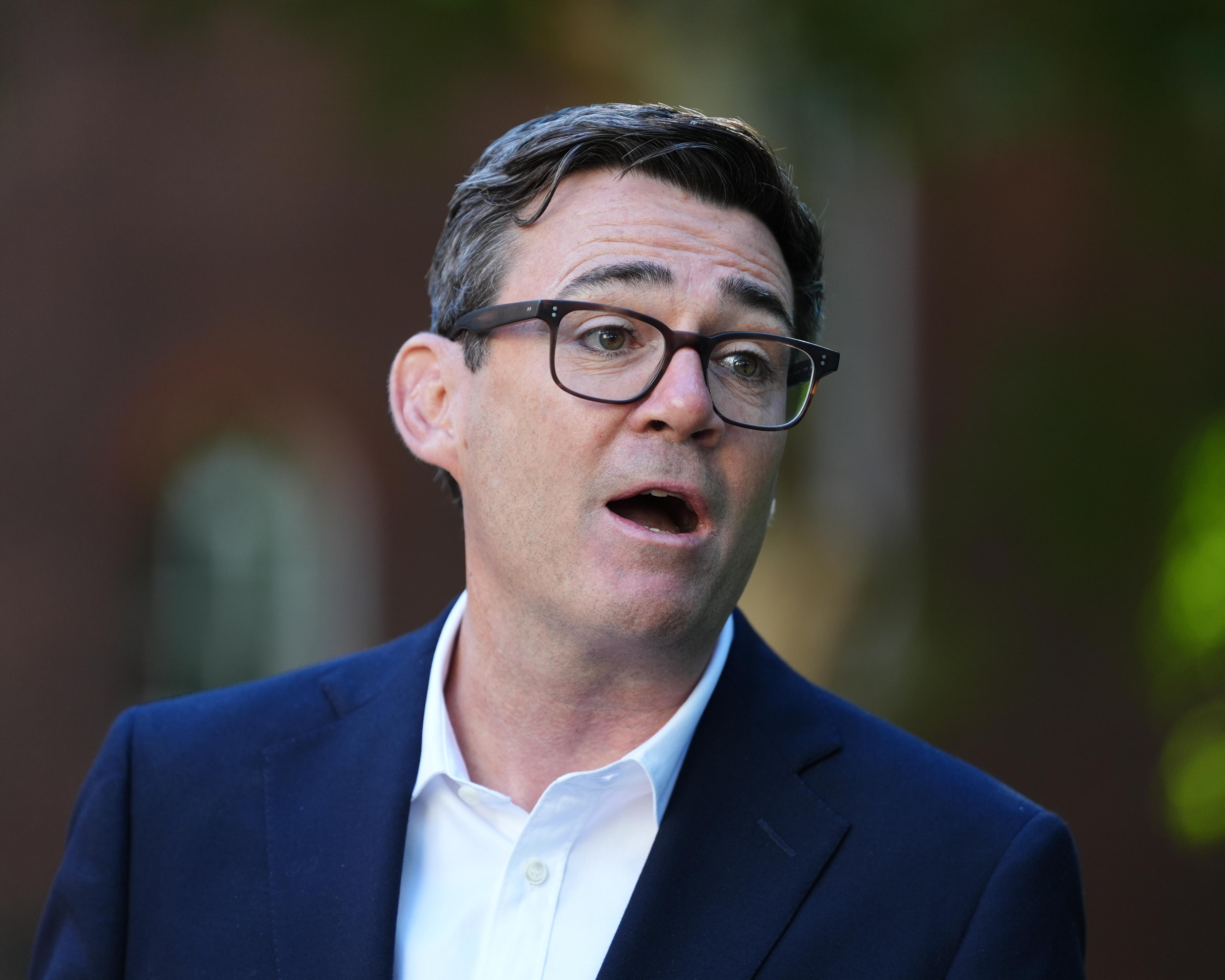A man in glasses and a navy suit speaks against a dark, blurred background.