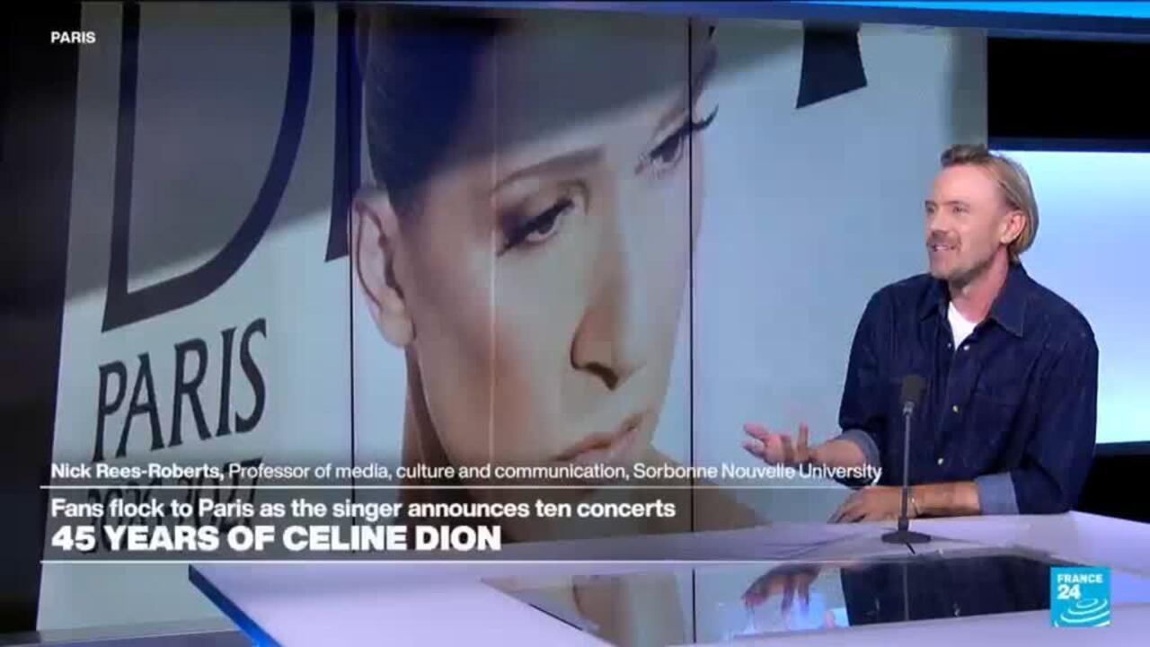 Television presenter seated in a studio beside a large portrait of Céline Dion.
