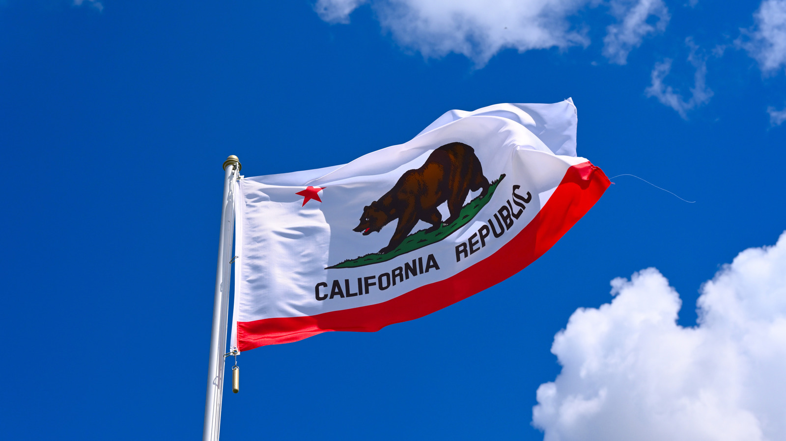California state flag waving on a flagpole against a vivid blue sky with white clouds