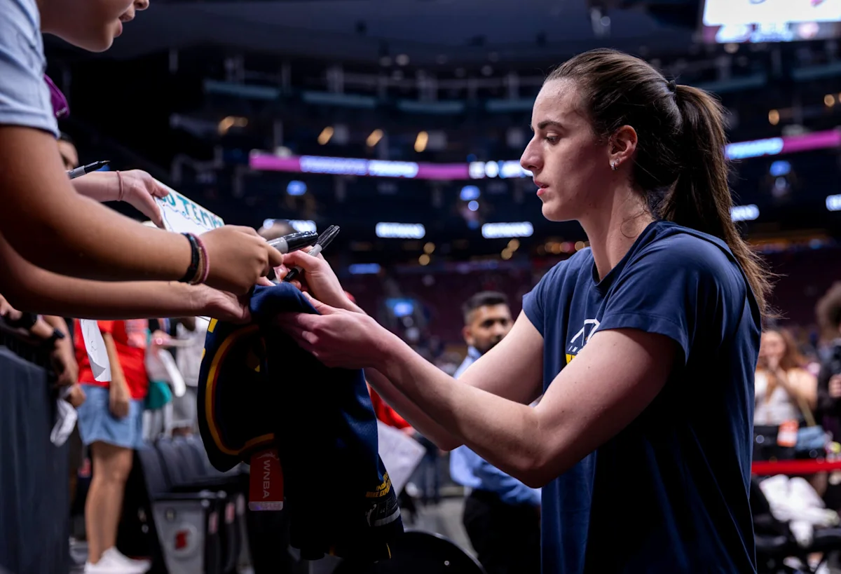 Basketball player signs autographs for fans courtside during a game