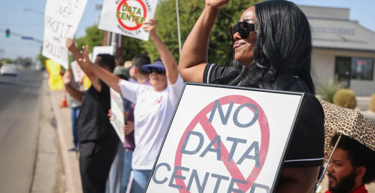 Protester holds a framed “No Data Center” sign during a roadside demonstration.