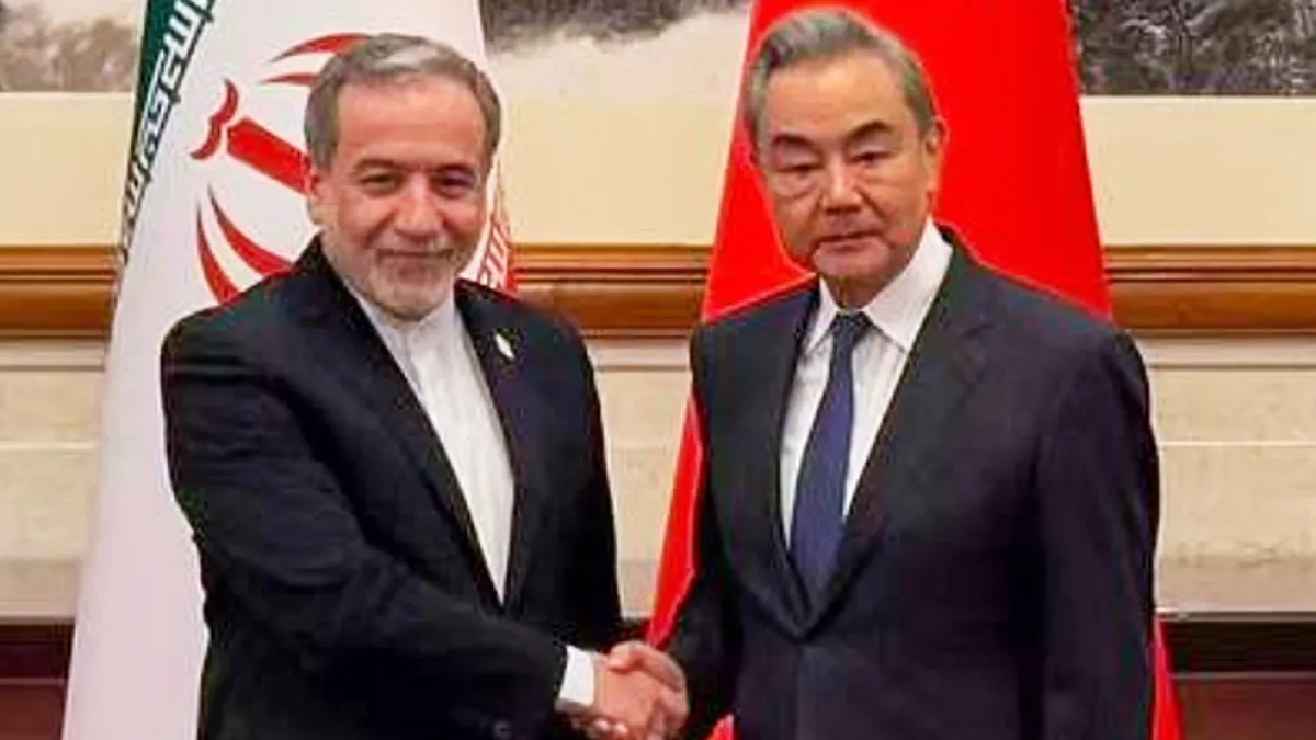 Two suited men shake hands in front of Iranian and Chinese flags.
