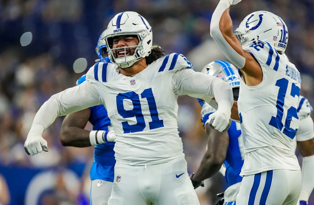 Colts football players in white uniforms celebrate during a game, with defensive player number 91 in foreground